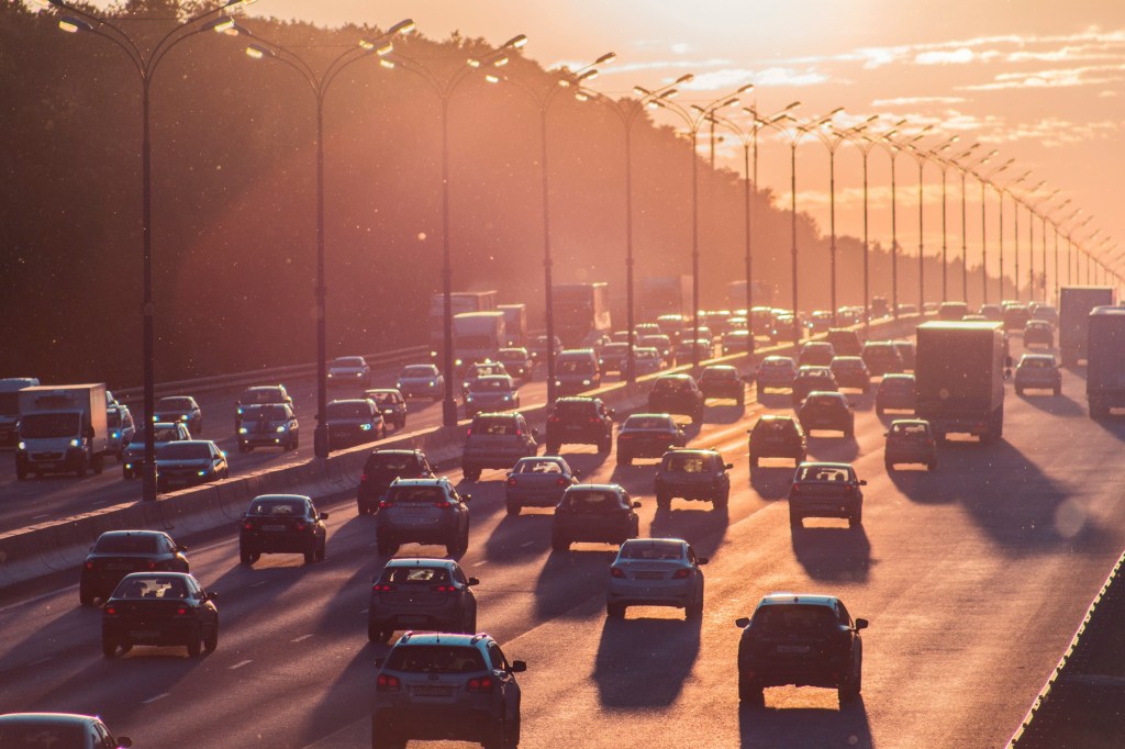 Traffic on a highway during sunset, with various cars and trucks visible under streetlights.