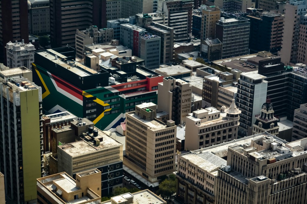 Aerial view of a cityscape featuring buildings and a prominent mural showcasing the South African flag on a structure.